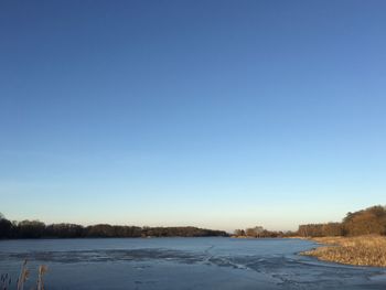 Scenic view of lake against clear blue sky during winter