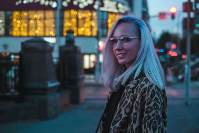 Portrait of smiling young woman standing on city street at dusk