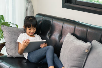 Girl learning over digital tablet while sitting on sofa at home