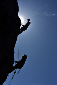 Low angle view of silhouette men climbing mountain against clear sky