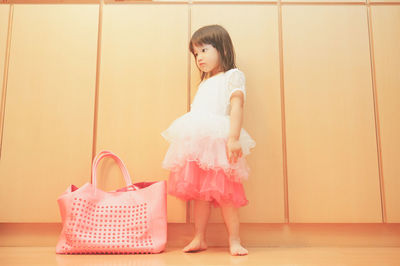 Cute girl standing by bag against wall at home