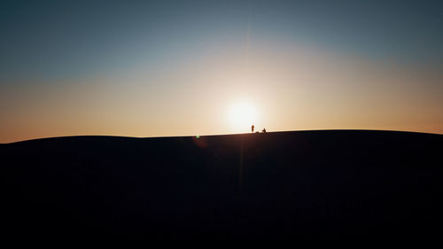 Silhouette people on landscape against sky during sunset