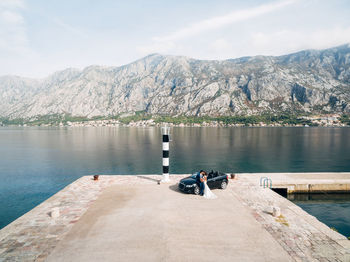 People on lake by mountains against sky