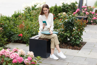 Yong women with laptop using mobile phone while sitting