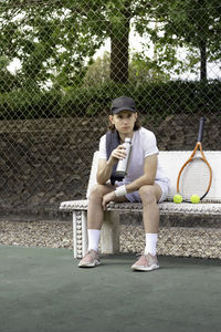 Young man resting sitting on a bench after playing a tennis match with a bottle of water