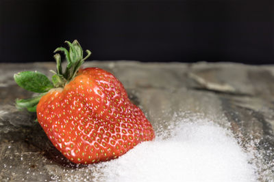 Close-up of strawberries and sugar on table against black background