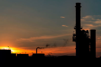 Silhouette factory against sky during sunset