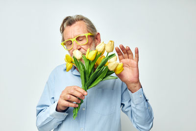 Portrait of senior woman holding flower against white background