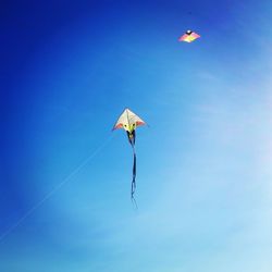 Low angle view of kites flying against clear blue sky