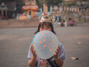 Portrait of young woman holding balloon while standing on road
