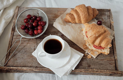 Tasty breakfast with fresh croissant, coffee, cherries on a wooden tray. hearty croissant 