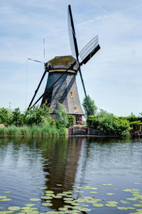 Traditional windmill by lake against sky