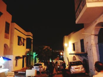 People on illuminated street amidst buildings at night