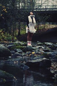 Full length of woman standing on rock in forest