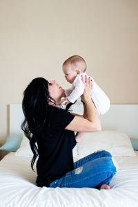 Charming brunette woman playing with her baby while sitting on bed