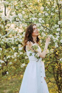 A cute happy young woman with a hairstyle in a white dress is walking enjoying nature in the summer