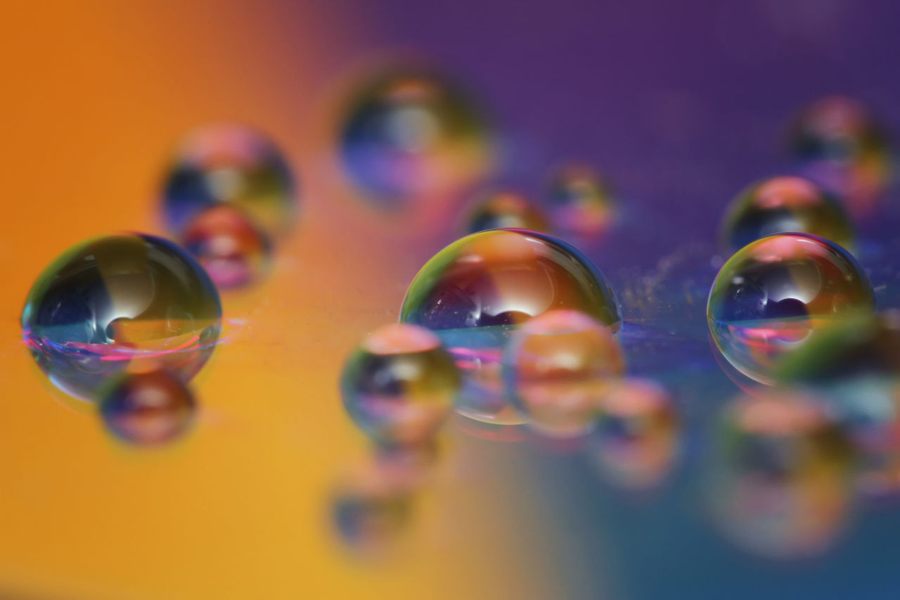 macro photography, close-up, multi colored, bubble, liquid bubble, selective focus, blue, drop, no people, fragility, yellow, reflection, flower, indoors, soap sud, mid-air, petal, water, nature, sphere, studio shot, colored background, marble, circle, focus on foreground