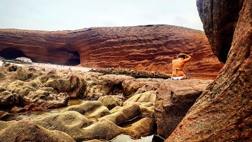 Rear view of young woman standing on cliff against sky