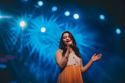 Full length of young woman standing against illuminated lights