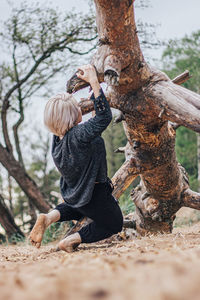 Full length of woman hanging on fallen tree at forest