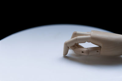 Close-up of wooden figurine hand on white table against black background