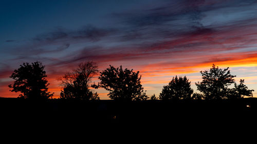 Silhouette trees against dramatic sky during sunset