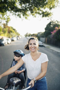 Portrait of happy woman holding bicycle with son sitting on back seat