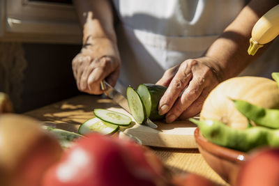 Senior woman cutting cucumber in kitchen