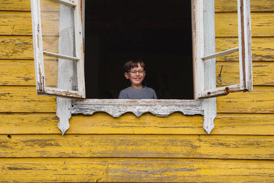 Portrait of smiling kid in a window of a yellow house