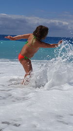 Young woman splashing water in sea against sky