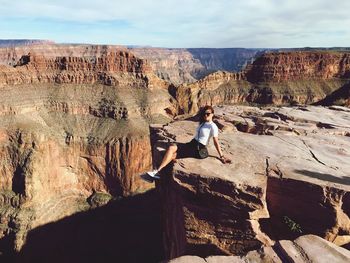 Full length of woman sitting on cliff against sky at national park