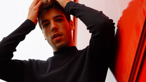 Low angle portrait of young man with hands in hair against wall