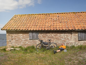 Cyclist relaxing near stone house at sea