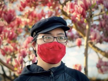 Portrait of man in cap, eyeglasses and face mask against pink flowering magnolia tree.