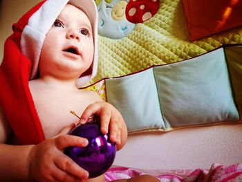 Close-up of thoughtful baby girl wearing santa hat while sitting on bed at home