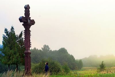Man on field looking at cross sculpture
