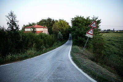 Road sign by trees against sky in city