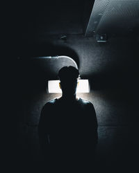 Rear view of silhouette man standing against dark wall