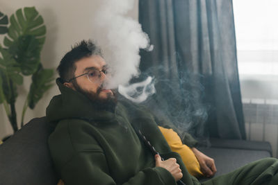 Young man looking away while sitting on sofa at home