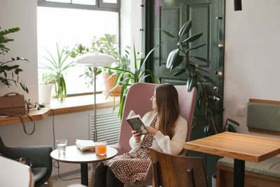 Young woman reading a book while sitting at home or in cozy hipster cafe, candid lifestyle