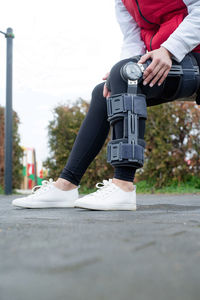 Woman wearing sport clothes and knee brace or orthosis after leg surgery, walking in the park