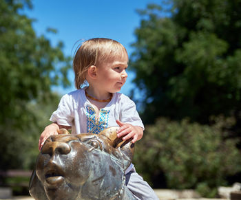 Low angle view of boy sitting on animal statue at park