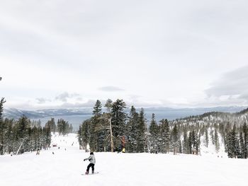 Man snowboarding on snow covered field against sky