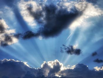 Low angle view of sunlight streaming through clouds