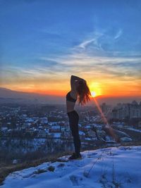 Side view of woman with hands in hair standing against sky during sunset