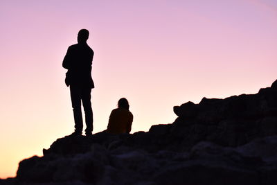 Silhouette people standing on rock against sky during sunset