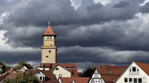 Medieval tower amidst buildings against dark clouded sky