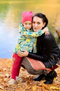 Portrait of mother with daughter by lake during autumn