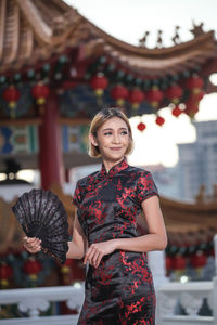 Smiling young woman wearing traditional clothing while holding hand fan