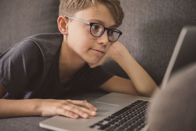 Boy using laptop while relaxing on sofa at home